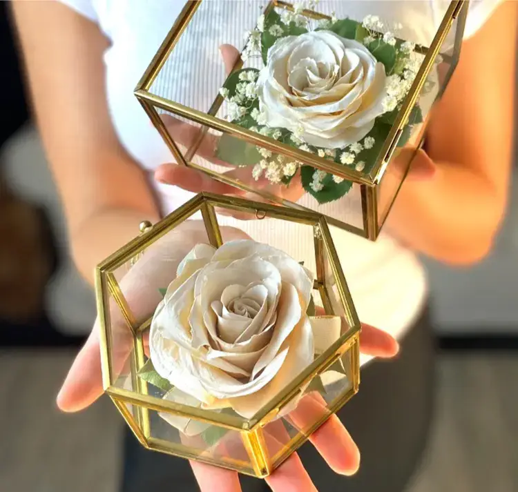 Two preserved wedding flower keepsakes--a single white rose in a hexagonal and square box.